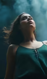 a woman in a green tank top looks upward as she smokes