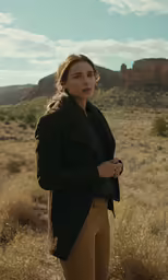 a woman wearing brown pants stands in a field