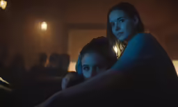 two girls are sitting in a dark room looking at something on the screen