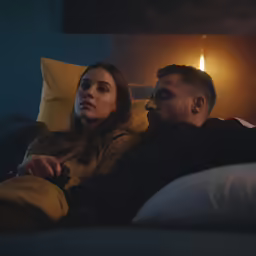 a man and woman sitting on a couch watching television