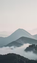 the clouds are moving over the mountains and a few trees