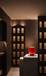 an illuminated red vase stands on top of the white pedestal
