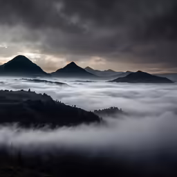 dark clouds surround a forest and mountains with a sun setting behind it