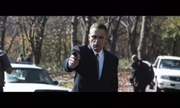 a young man dressed in a suit pointing a gun at someone
