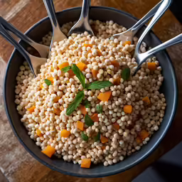 the bowl contains white couscous with carrots and green leaves