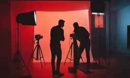 two men in front of camera equipment that is red