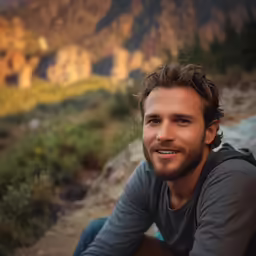 a close up view of a man with a beard, wearing a gray shirt and jeans