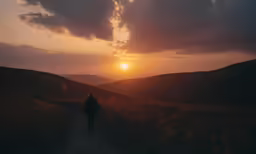 a woman is standing alone in the field as the sun sets