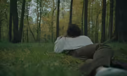 a woman laying in a field of grass in the woods