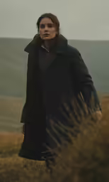 a man is standing on top of a hill, in a coat