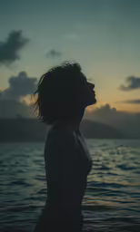 a woman standing in the water at dusk