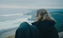 a woman standing on the edge of a cliff looking over water