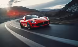 a red sports car driving on a road with the sun behind it