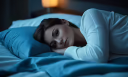 a woman laying in bed with blue sheets