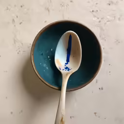 spoon with dirty painted handles sits inside of a blue bowl