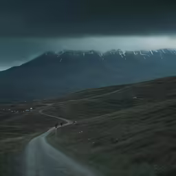 two people walking along a dirt road with mountains in the background