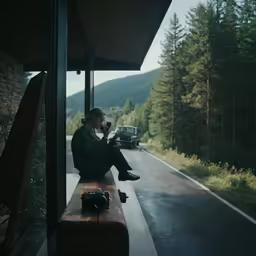 a man sits on the side of the road while holding a camera