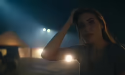 a young woman stands in the dark, with her hands on her head