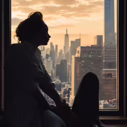 a person sitting in a chair looking out the window at the city
