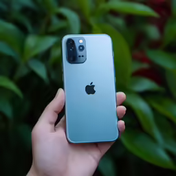 the hand is holding a silver apple phone in front of a bush