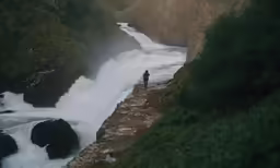 a person stands on a ledge in front of a waterfall