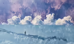 man stands on a snow covered hill looking out at the clouds