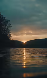 a sun reflecting off of water with hills in the background