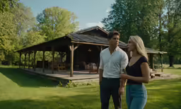a man and woman standing in a field next to a pavilion