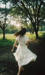 girl in white dress walking through grass towards trees