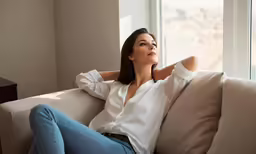 the woman is sitting on the couch near a window