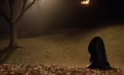 a woman sitting on the ground near a tree and lamp post