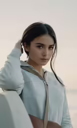 a woman wearing a sweatshirt stands next to a surf board