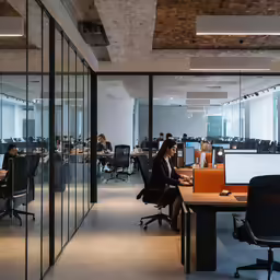 an office with large windows and a person sitting at a desk on the phone