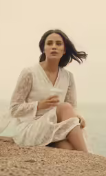 a woman in white dress sitting on the beach