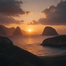 the sun rises above some big rocks off of the coast