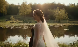 a bride stands near a lake and looks off at the sky