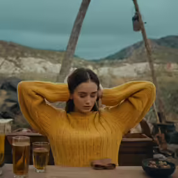 a woman wearing a yellow sweater is sitting by a table with beer