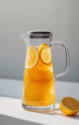 a pitcher filled with oranges and sitting next to two slices of lemon