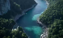 a wide river surrounded by green trees, in the middle of mountains