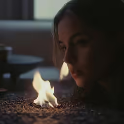 a woman looking at a lit candle in the middle of a room
