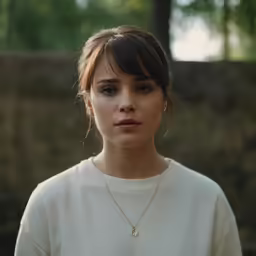 a woman wearing white shirt and gold necklace standing in front of trees