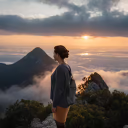 a woman is standing at the top of a mountain overlooking the clouds