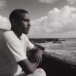 a man sitting on the rocks looking at the ocean
