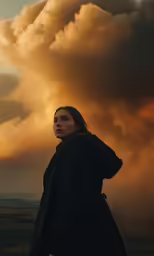 a woman standing in the grass under a large cloud