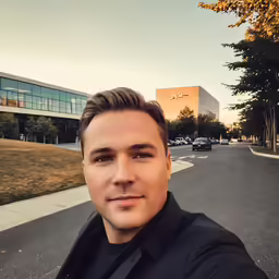 man in tuxedo taking selfie on street in front of large office building