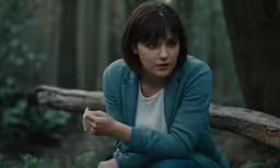 a woman sitting on a log in the woods