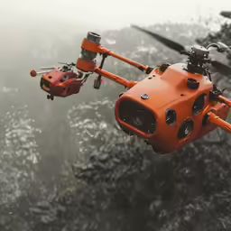 an orange helicopter hovers above a tree covered forest