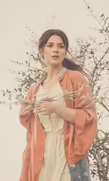 a woman in a dress holding flowers against the background of a bare tree