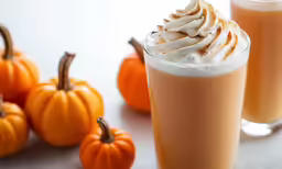 two beverages in glass sitting next to small orange pumpkins