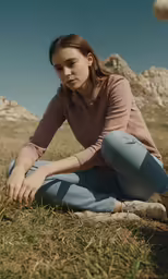 a woman wearing jeans and brown shirt sitting in the grass